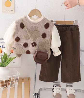 Ensemble bébé automnal mixte avec haut écru à manches longues, gilet tricoté à pois et pantalon marron côtelé, parfait pour un style vintage et confortable.