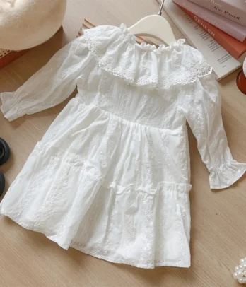 Robe blanche raffinée en broderie anglaise avec col Claudine volanté, motifs floraux délicats et coupe évasée, parfaite pour les grandes occasions.