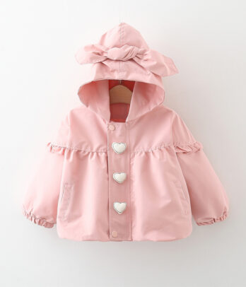 Coupe-vent enfant rose à capuche avec nœud décoratif, imprimé de cœurs blancs, manches longues à poignets élastiqués et double fermeture zip et boutons-pression, en tissu léger pour la mi-saison.