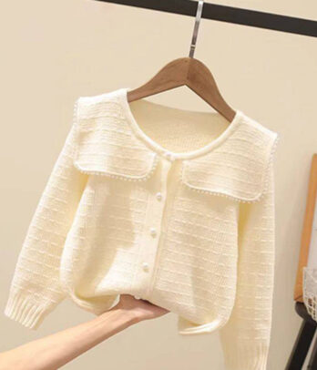 Cardigan fille style old money en maille blanc cassé avec col volanté romantique, fermeture boutonnée sur le devant et coupe sophistiquée, idéal pour les tenues élégantes.