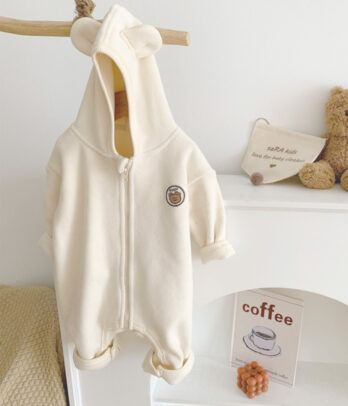 Combinaison pour bébé blanc cassé à capuche avec petites oreilles, en tissu doux et molletonné. Fermeture zippée ou à boutons pour un habillage facile. Un vêtement mixte, confortable et chaud, idéal pour l’hiver.