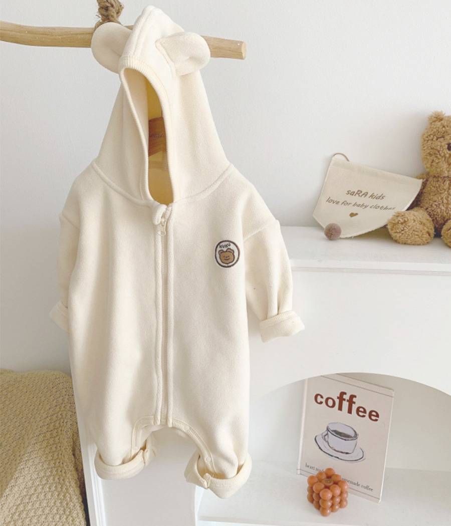 29111 Combinaison pour bébé blanc cassé à capuche avec petites oreilles, en tissu doux et molletonné. Fermeture zippée ou à boutons pour un habillage facile. Un vêtement mixte, confortable et chaud, idéal pour l’hiver.
