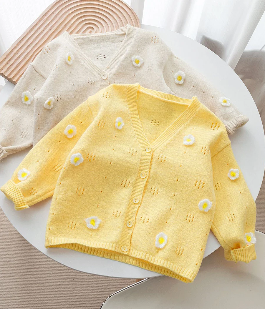 43177 Gilet enfant en tricot jaune pastel orné de fleurs blanches brodées, coupe légère avec boutons discrets sur le devant, idéal pour le printemps et la mi-saison.