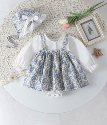 Barboteuse bébé style robe et chemise, avec jupe à imprimé floral délicat, haut chemise blanc à col classique et manches longues, matière souple et respirante, et fermeture à boutons-pression pour un habillage facile.