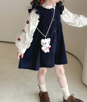 Ensemble fille rétro avec blouse blanche manches longues à broderies florales rouges et col froncé, robe chasuble bleu nuit évasée à boutons.