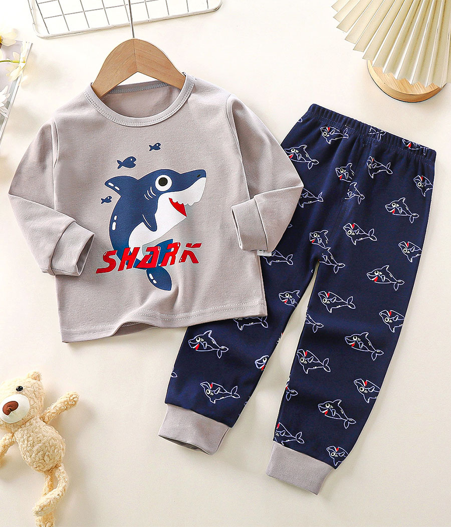 89578-4 Pyjama deux pièces pour garçon composé d’un haut bleu clair à manches longues avec un grand motif central de petit requin, col rond et finitions confortables, associé à un pantalon bleu foncé uni à taille élastiquée et bas resserrés, confectionné dans un tissu doux et respirant pour des nuits cosy et amusantes sur le thème marin.