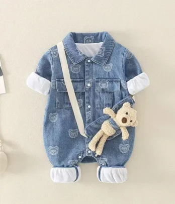 Combinaison bébé en jean clair avec imprimés enfantins, bretelles réglables, poche avant ornée d’un petit nounours amovible, style décontracté et ludique parfait pour les sorties et les jeux.