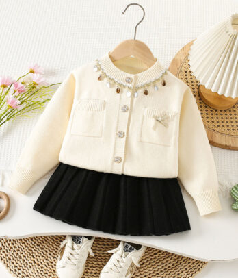 Ensemble fille 2 pièces avec cardigan crème orné de perles et pampilles dorées, poches plaquées et broche nœud, jupe noire plissée à taille élastique, matière douce et chaude.