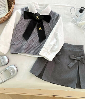 Ensemble classique pour fillette avec gilet tricoté gris à boutons, chemise blanche à col chic et jupe assortie à nœud décoratif, idéal pour les occasions élégantes.