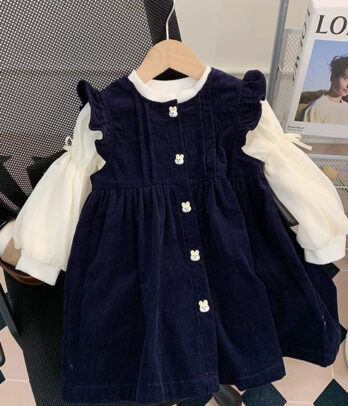 Ensemble pour enfant composé d’une robe trapèze en velours bleu à boutons et d’un pull blanc cassé en maille fine à manches bouffantes, chic et confortable.